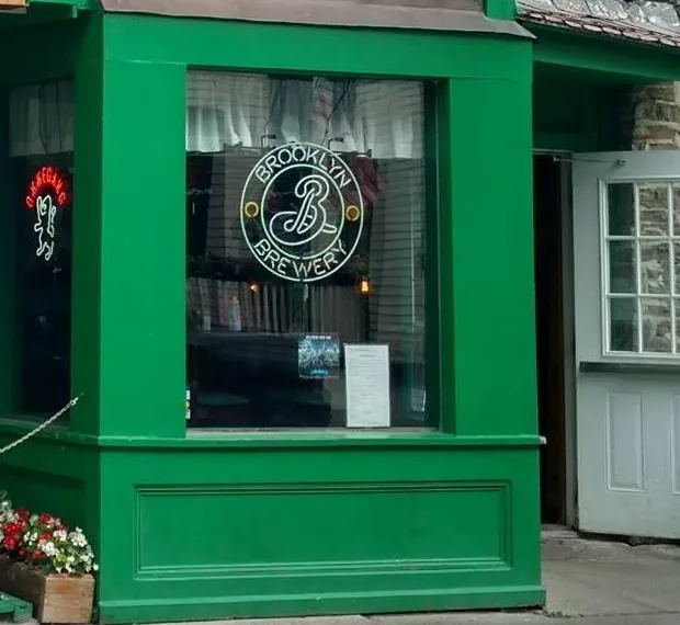 The bay window at Cooley's with a Brooklyn Brewery neon sign lit inside and the menu taped to the glass